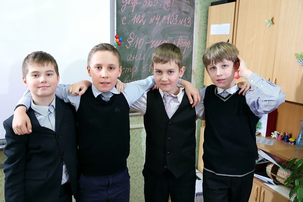 Четверо одноклассников в школьной форме обнялись в классе