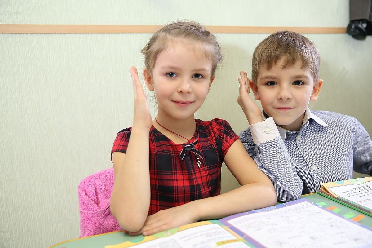 Первоклассники за партой тянут руки