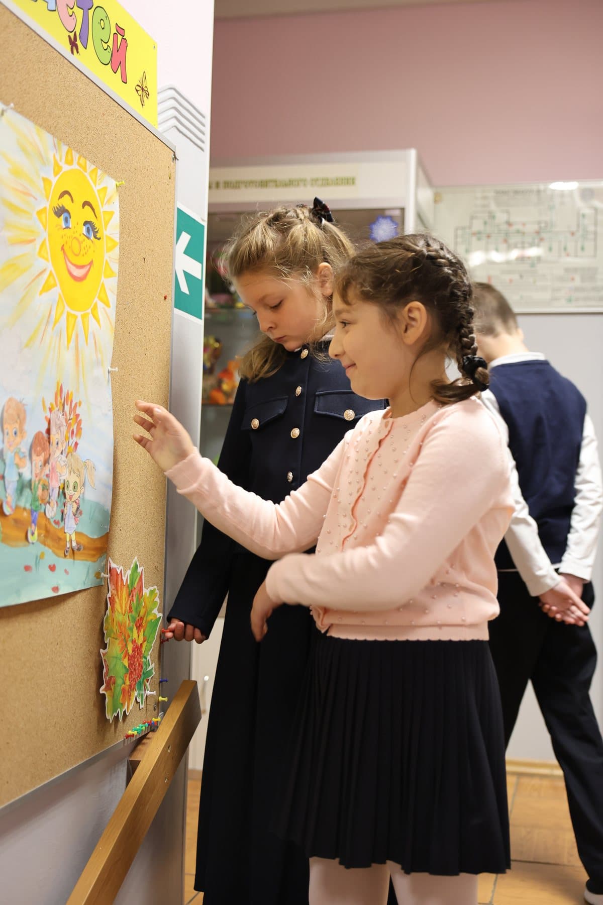 Ученицы рассматривают рисунки на стенде в коридоре школы